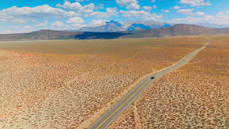 lonely black car on the road to nevada, usa. beautiful sight of desert contrasting with blue skies. mountains at backdrop.