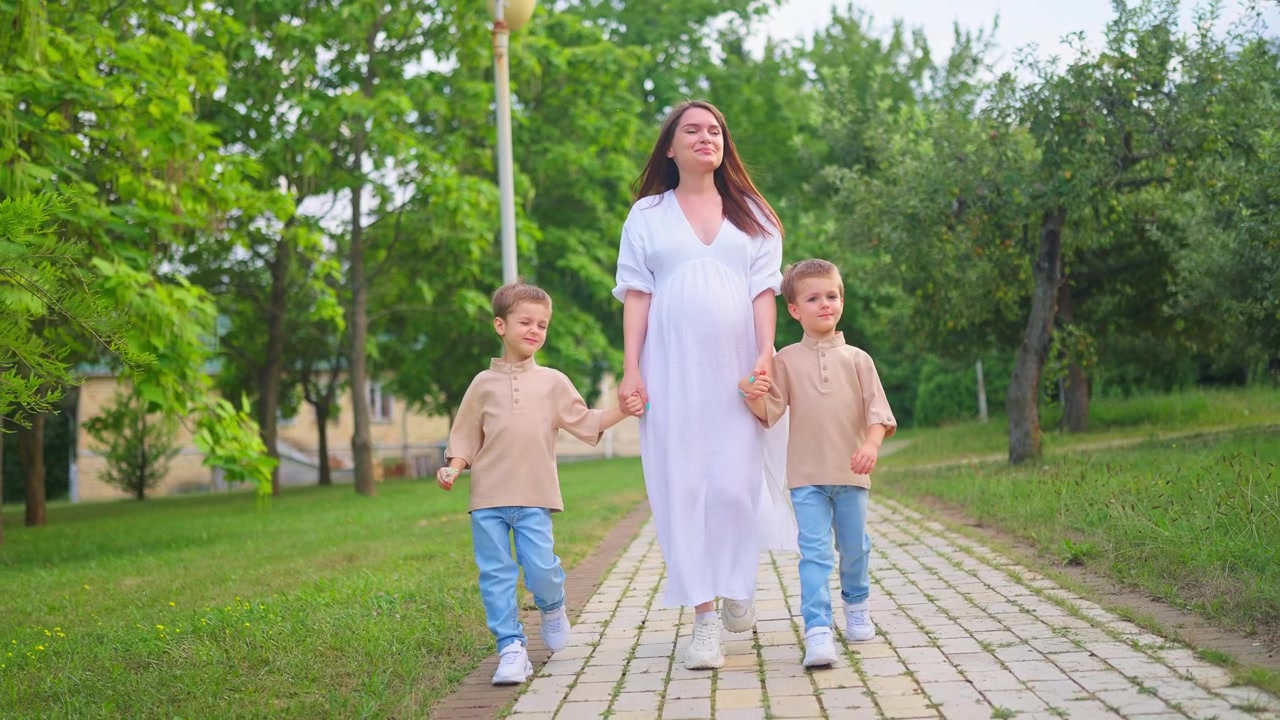 Zwangere vrouw loopt hand in hand met haar twee jonge zoons in een park