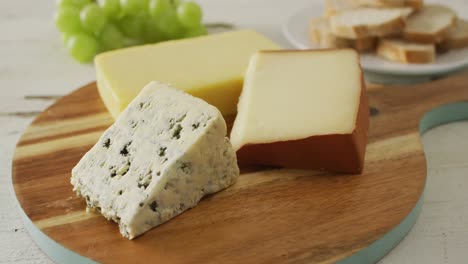 video of assorted cheeses on chopping board, with grapes and bread on rustic wooden table