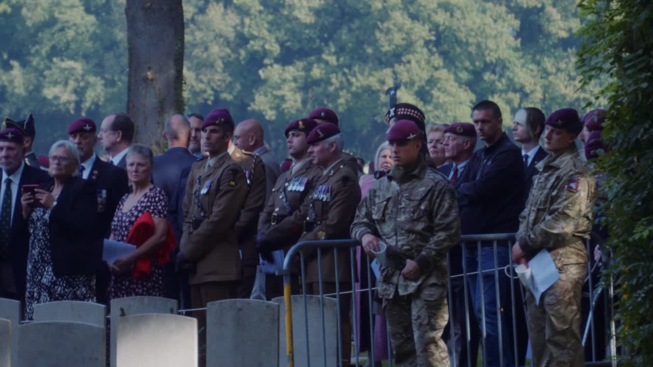 Soldiers and veterans stand solemnly during a memorial ceremony at Oosterbeek War Cemetery. The image captures the formal atmosphere of honoring fallen soldiers. Oosterbeek, Gelderland, Netherlands