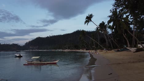 Einfacher-Lebensstil-Und-Ländliche-Dorfatmosphäre,-Wenn-Kinder-Abends-Am-Strand-Von-Port-Barton-Mit-Einer-Palmenseilschaukel-Spielen