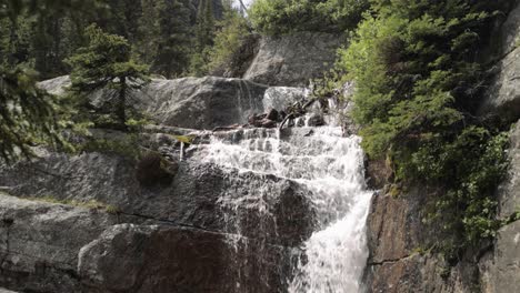 beautiful waterfall cascading down a rock face on the hiking trail up to lake agnes tea house on mount st. piran and mount whyte, within banff national park near lake louise alberta.