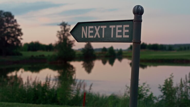 Cartello del tee del campo da golf in un parco da golf vuoto. Mostra la direzione verso un lago naturale al tramonto