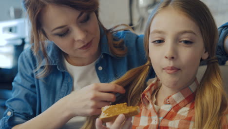 portrait shot of the charming mother and cute daughter sitting and having rest while eating bread with peanut butter and drinking juice and tea. close up. indoor