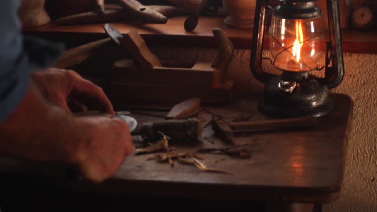 hombre de campo que trabaja con madera en su antiguo taller cerca de una linterna de aceite de metal vintage en un lugar de trabajo de madera