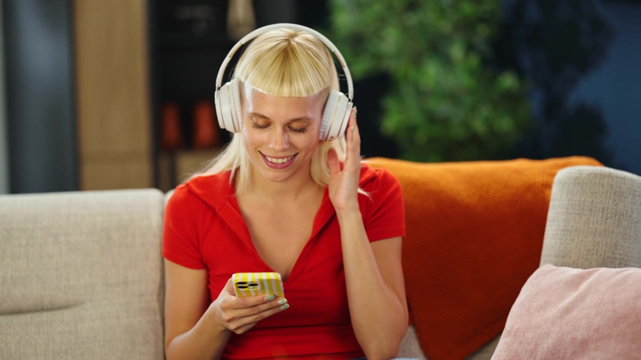 Giovane donna che indossa le cuffie e usa lo smartphone sul divano