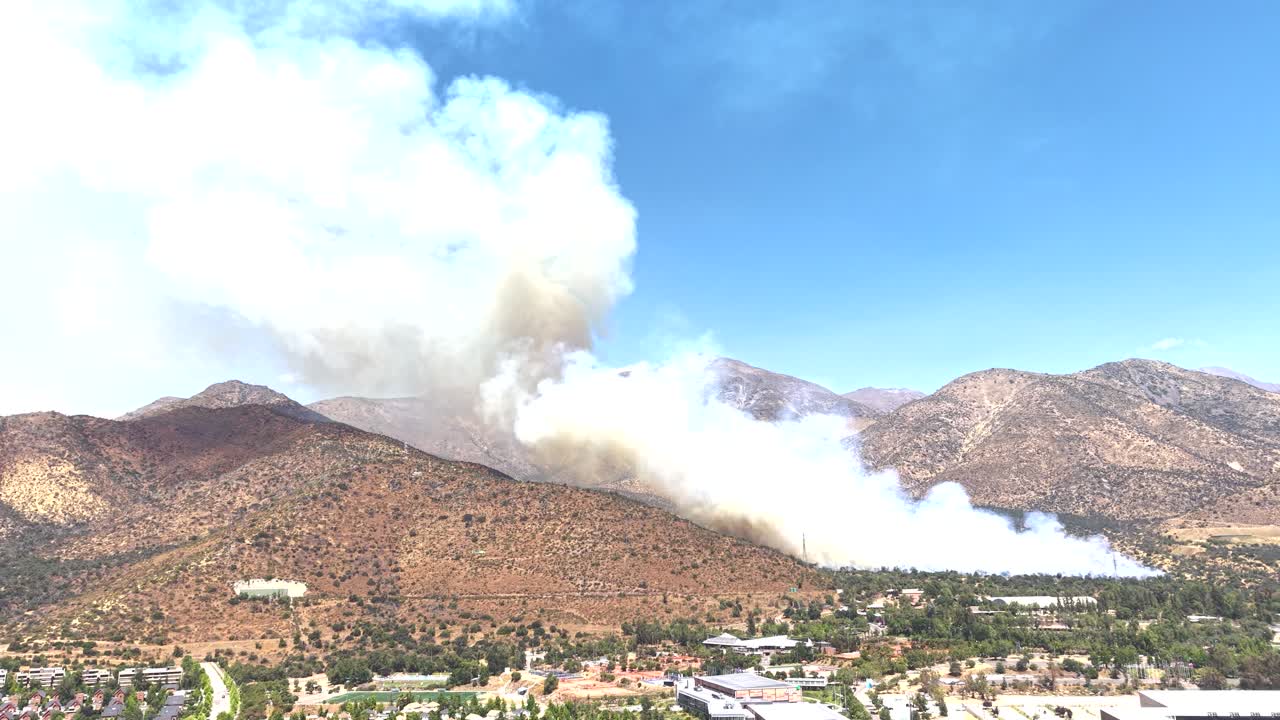 チリの都市の建物や山々の近くで立ち上る大規模な山火事の煙のプルームの空撮ドローンビュー、4K。