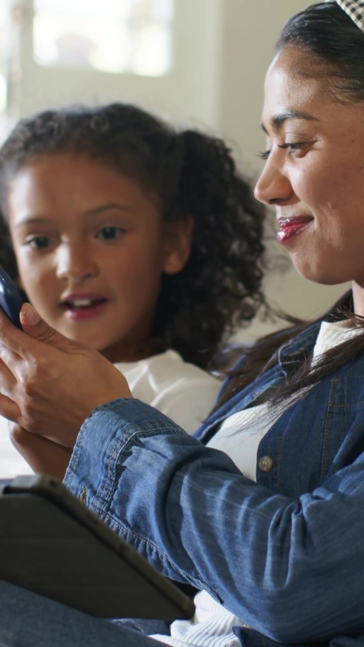 Video verticale: Bambino che tocca e gira il telefono verso la mamma a casa, mostrando lo schermo mentre la mamma usa il tablet