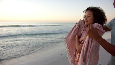 biracial couple enjoys a serene beach sunset, wrapped in a cozy blanket, with copy space