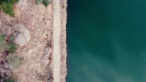 traveling areal drone shot looking down at a bike path beside still water
