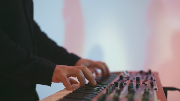 Close-up of a keyboardist's hands playing a red sampler piano against a soft pink and blue background