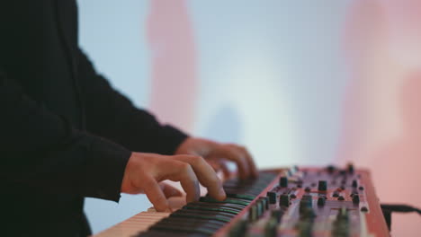 close-up of a keyboardist's hands playing a red sampler piano against a soft pink and blue background