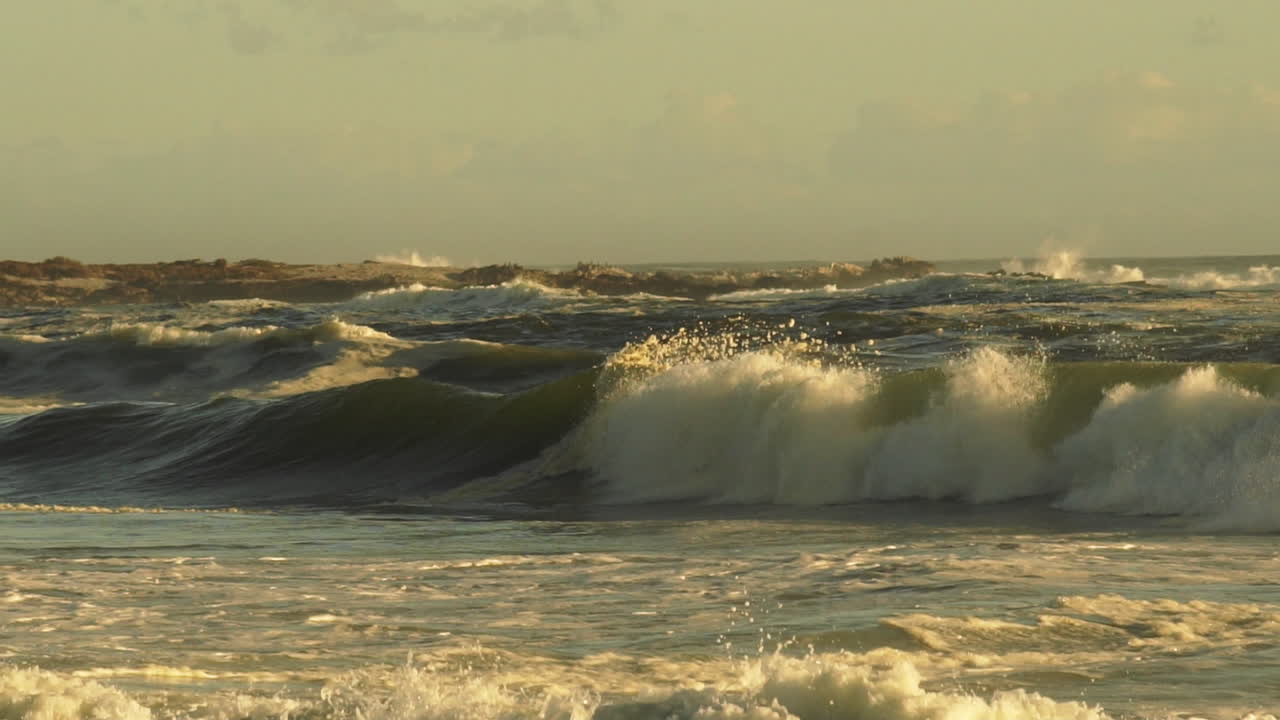 las olas violentas del mar que crean salpicaduras y espuma durante la tarde dorada - disparo de panela media