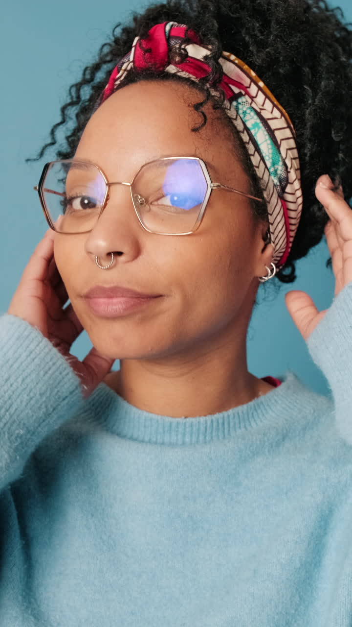 Smiling Young Woman with Curly Hair Adjusting Headscarf and Glasses