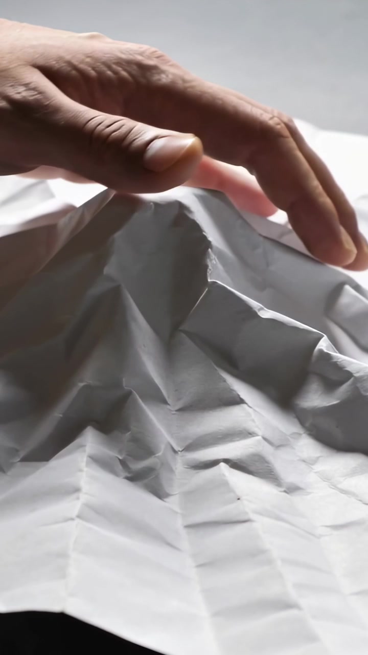 Vertical video: Entering right hand pressing and pinching white grid paper on table, shaping peak