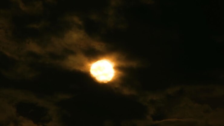 Huge orange full moon rises from behind cloudscape, time lapse