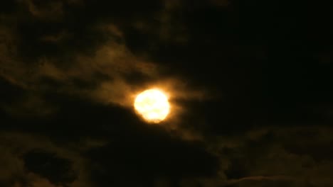 Huge-orange-full-moon-rises-from-behind-cloudscape,-time-lapse