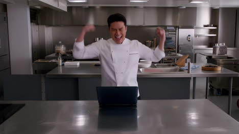 excited chef reacting to laptop in a professional kitchen