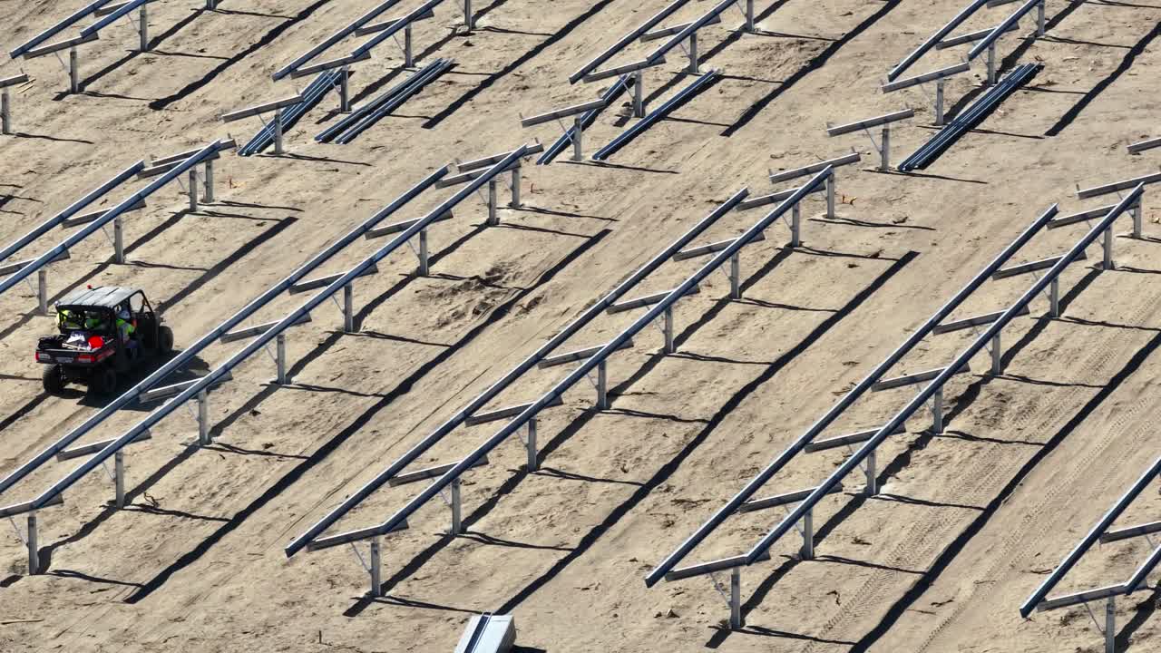 낮 동안 사막의 태양 패널 건설 현장에서 금속 프레임을 통해 운전하는 노동자를 운반하는 atv의 텔레포토.