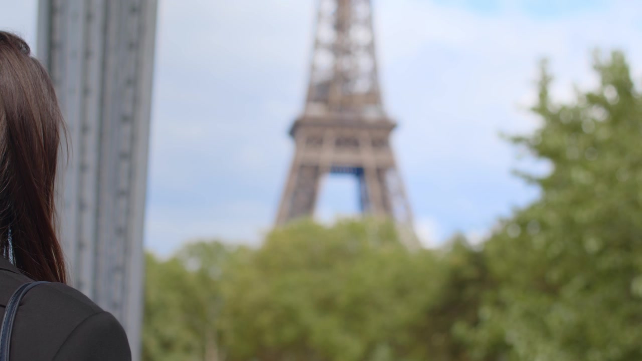 Donna bruna in piedi che guarda la Torre Eiffel in lontananza, Parigi, Francia.