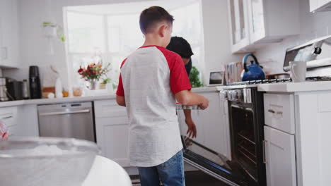 Pre-teen Hispanic boy baking with grandfather and father in kitchen, putting cakes in oven, close up