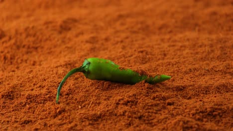 Slow-motion-whole-green-chilli-pepper-laying-on-pile-of-mixed-paprika-with-chilli-powder-sprinkled-over-the-top