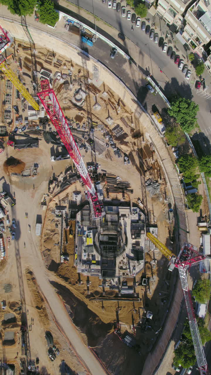 Vertical top down over Tower Crane in construction site on a big Square while cars drive by - tel aviv, israel