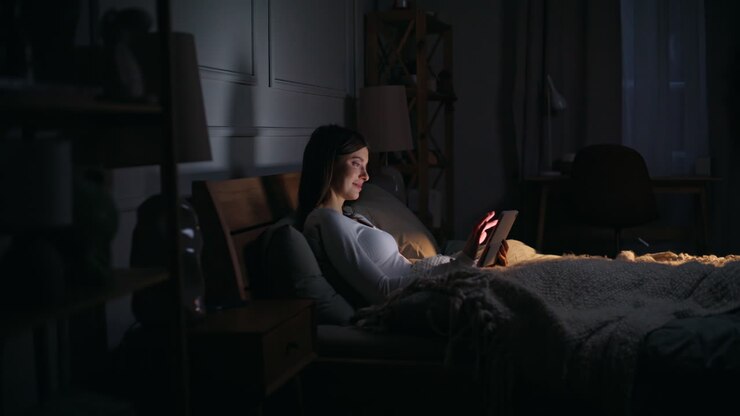 Donna a casa che tocca lo schermo luminoso del tablet sdraiata comodamente nel letto di casa di notte