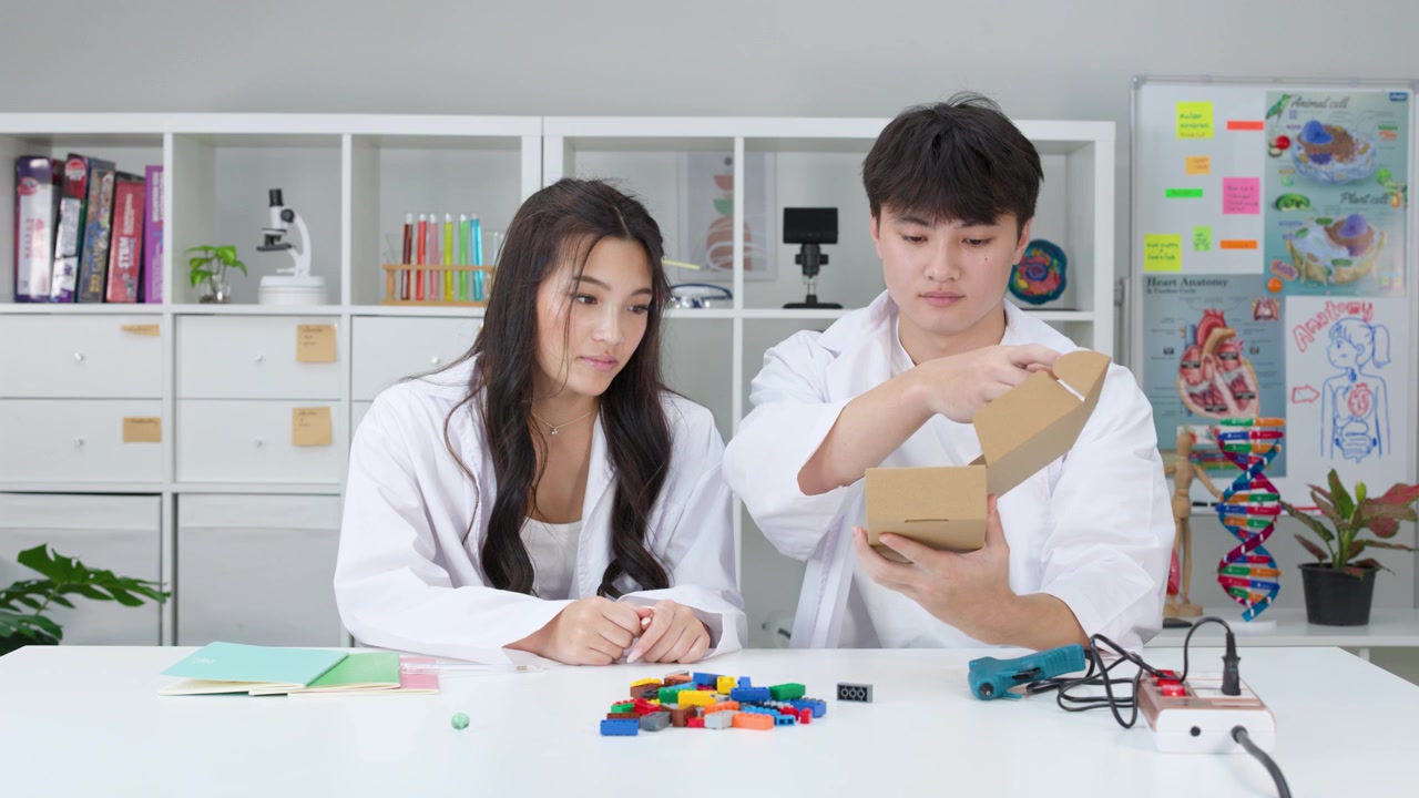 教室でのSTEM実験中、白い白衣を着た2人の学生が段ボール箱を調べている。