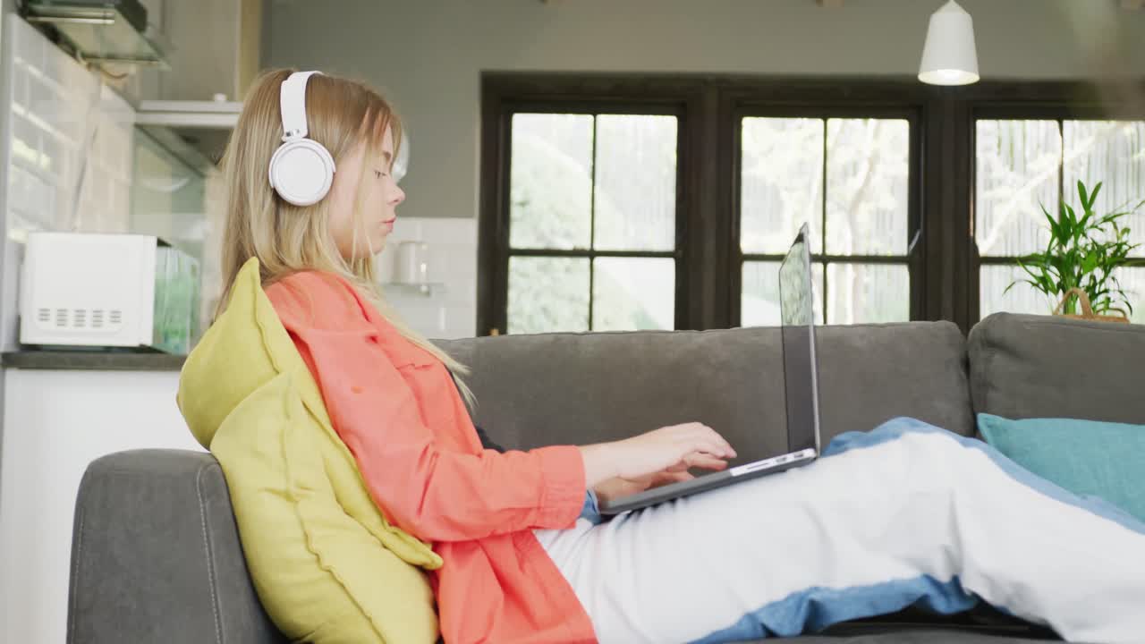 헤드폰을 끼고 집에서 노트북을 사용하는 백인 십대 소녀, 슬로우 모션