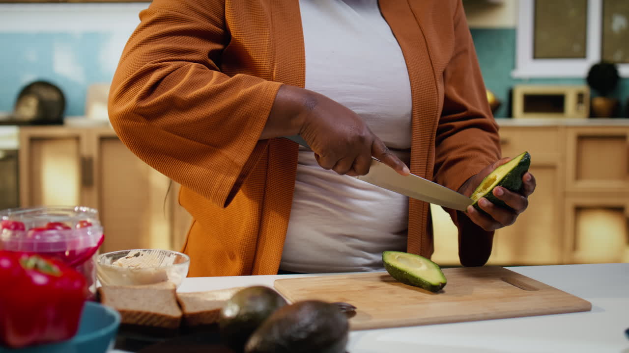 Content creator nero che taglia l'avocado in un video culinario al bancone.