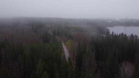 Imagen-De-Un-Dron-Descendiendo-Desde-Lo-Alto-Y-Apareciendo-De-La-Niebla-Mientras-Descubre-Un-Enorme-Lago,-Un-Bosque-Y-Una-Fábrica-En-La-Distancia