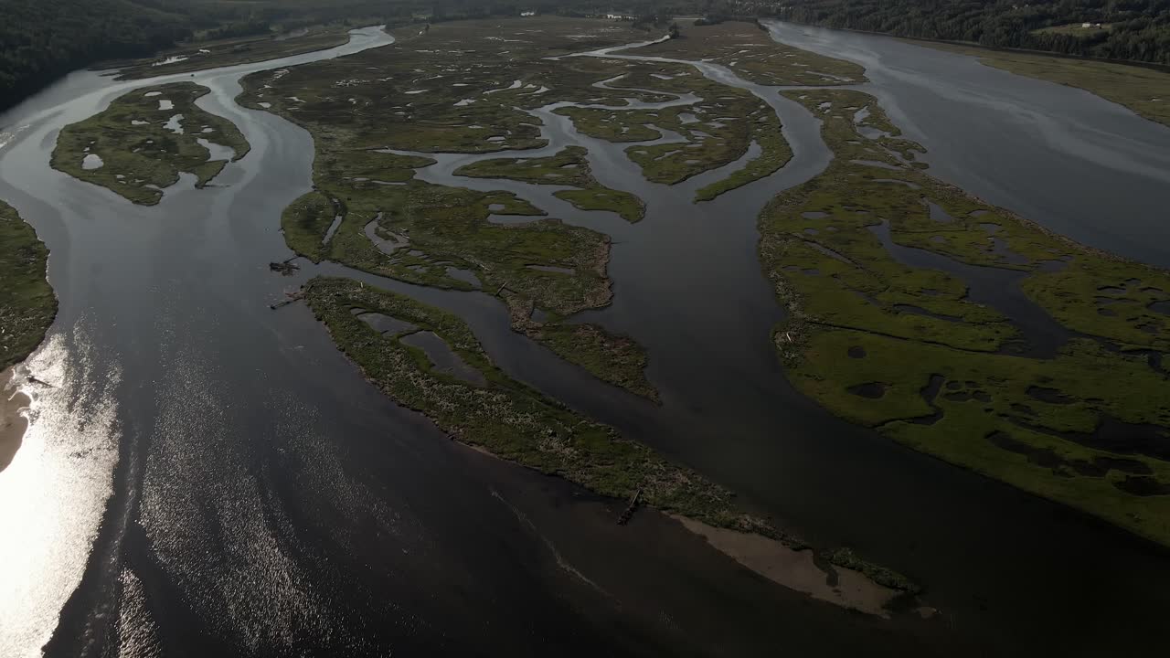 un dron que vuela sobre un río tranquilo que refleja la luz del sol durante el día se inclina hacia arriba y revela un pintoresco valle verde y montañoso en la bahía de gasp?