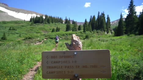 hiking sign on conundrum hot spring trail and woman with backpack in green landscape of rocky mountains, colorado usa, full frame