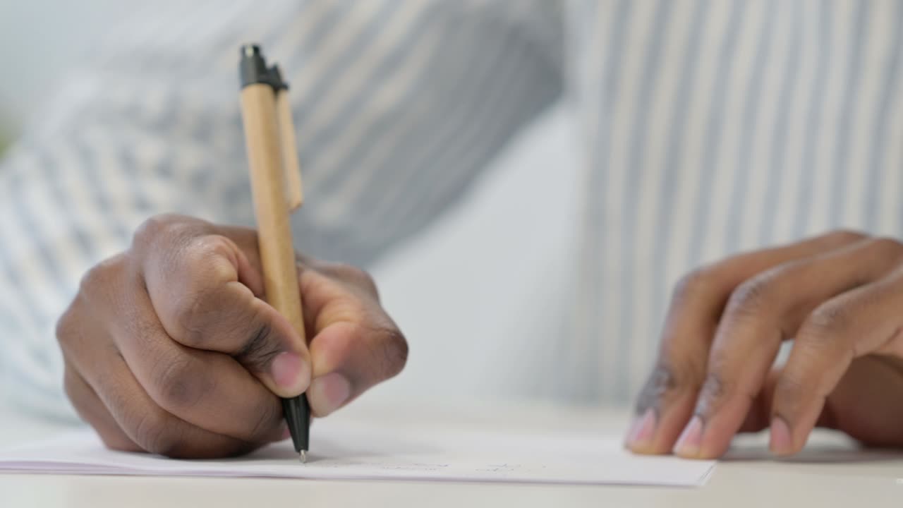 primer plano de un hombre africano escribiendo en papel con pluma