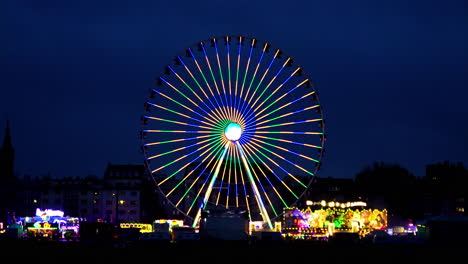 Toma-Manual-Estática-De-Una-Rueda-De-Ferris-Brillante-En-Diferentes-Colores-En-Un-Festival-En-Colonia-En-Alemania-Con-Otros-Paseos-Y-Atracciones-Brillantes-Por-La-Noche