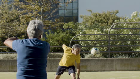 senior football player hitting ball with head while the goalkeeper catching it