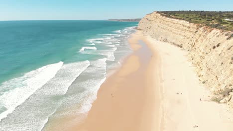 sandy beach of porto de mós by rocky cliff in lagos coast, algarve, portugal - aerial wide fly-over shot
