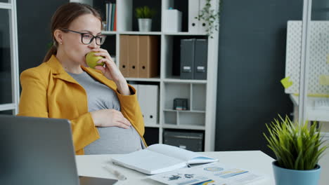 pregnant woman eating an apple in the office