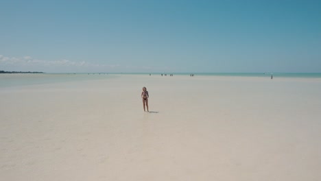 foto de seguimiento de una chica con bikini caminando en una playa de arena bajo el sol, holbox