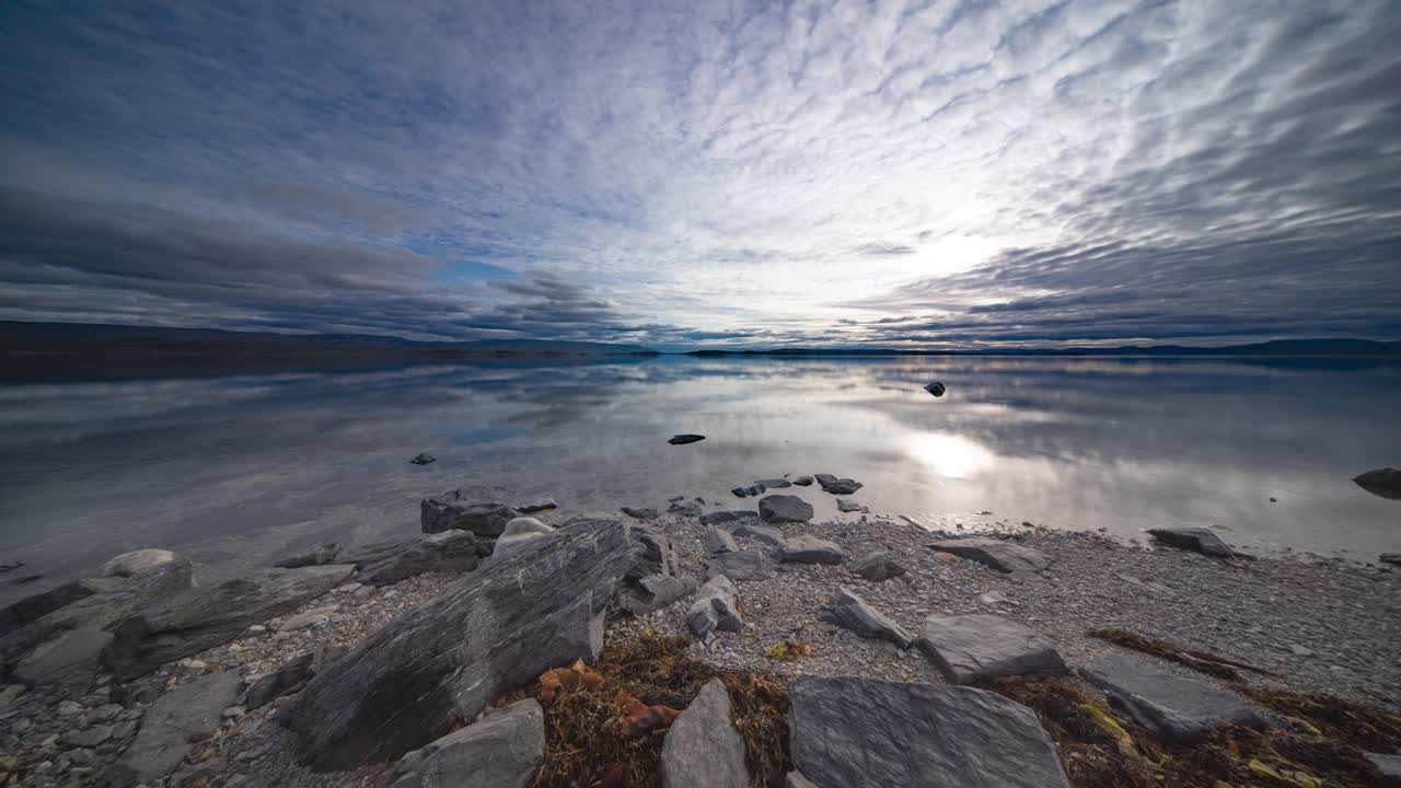 a medida que la marea se eleva lentamente, las nubes tormentosas se mueven rápidamente y se reflejan en la superficie espejo del fiordo, capturadas en un video de lapso de tiempo