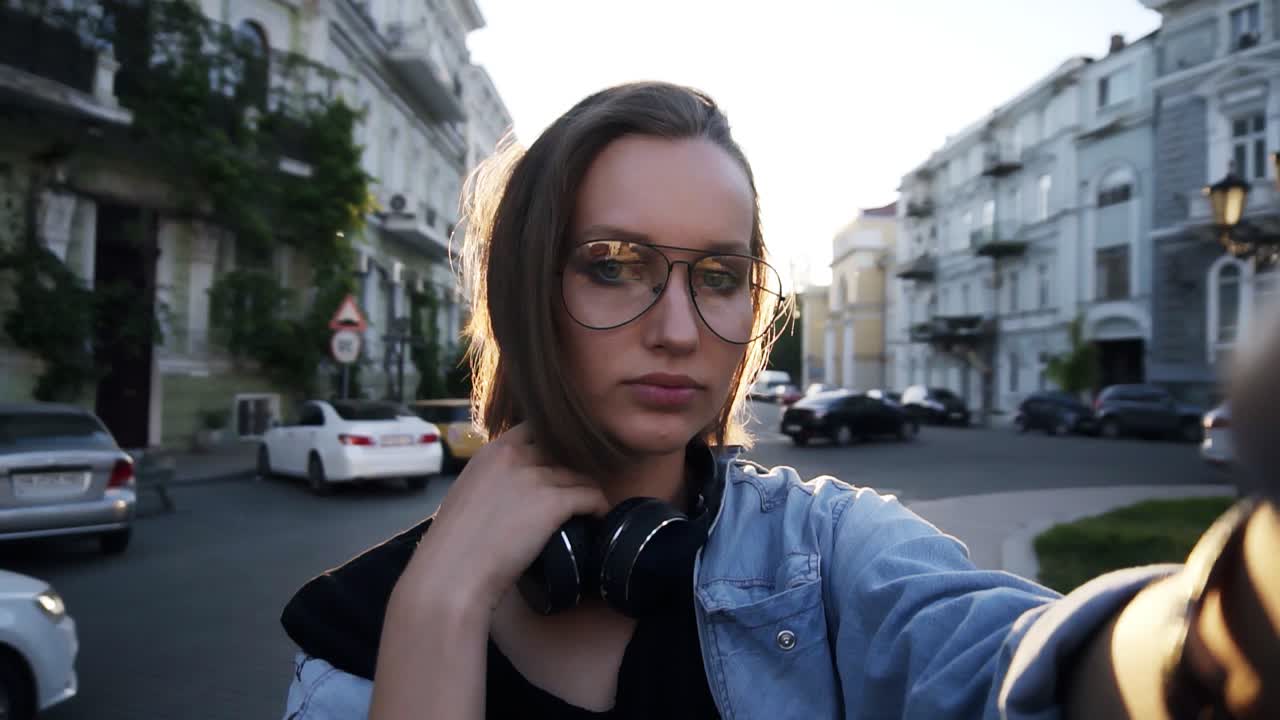 Portrait of and attractive girl with outstretched hand posing for camera, corrects her short hair. Headphones on her neck, wearing