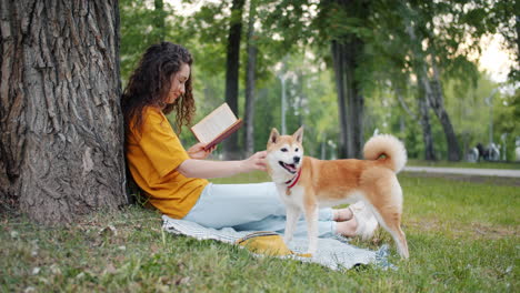 woman reading a book in the park with her dog