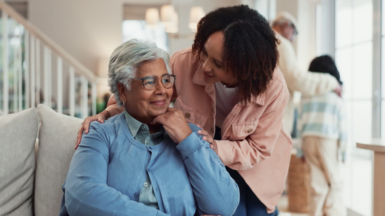 A happy grandmother and her daughter are smiling and looking at each other while sitting on a couch.