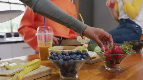 diversas adolescentes amigas con bebidas saludables cortando frutas en la cocina, cámara lenta