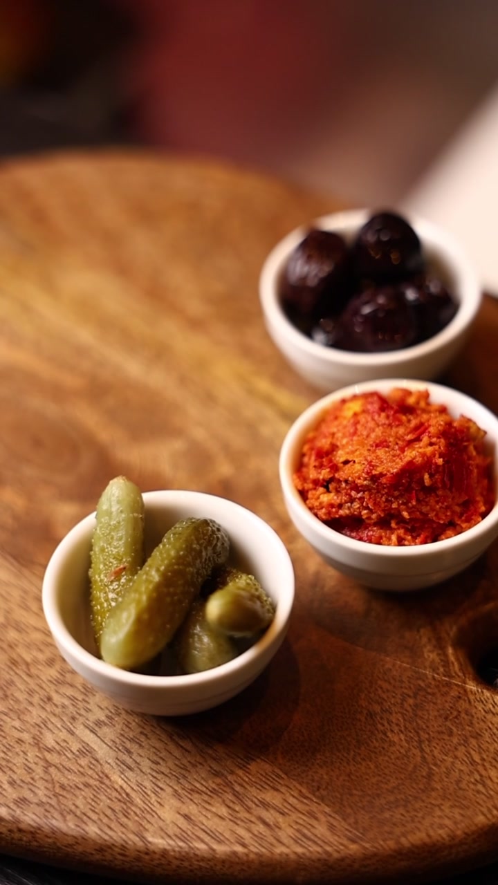 Small Bowls of Pickles, Olives, and Red Pepper Spread on Wooden Board