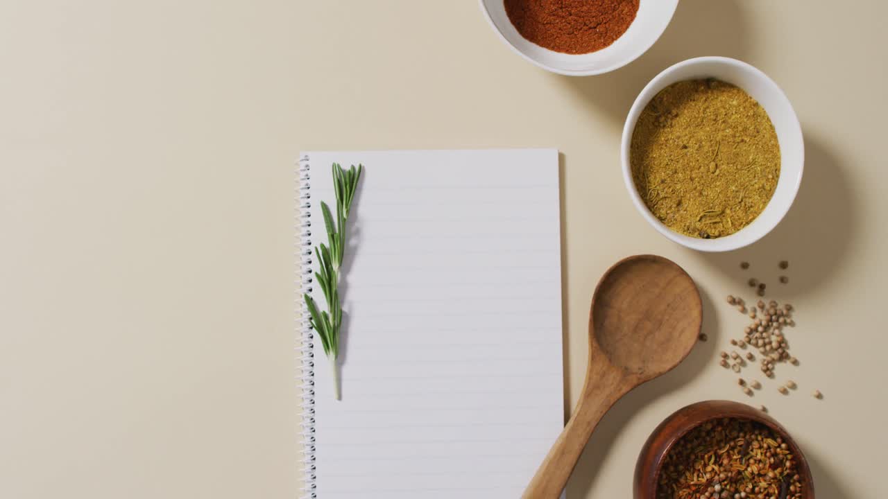 Video of spoon, notepad and bowls with diverse seasonings lying on beige surface