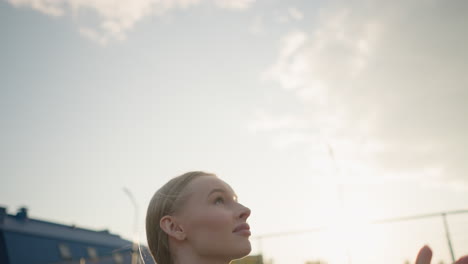 close up side view of lady in green sweater playing volleyball outdoors, hands raised to receive or pass ball with sunlight glow in background