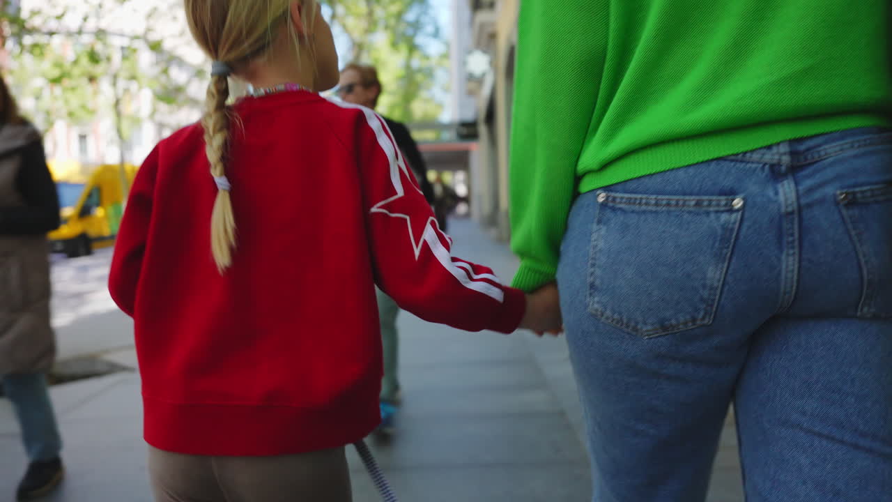 Mother and Daughter Walking Hand in Hand on City Sidewalk