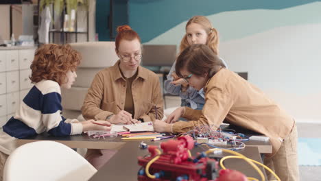 teacher and three schoolchildren drawing robot blueprint